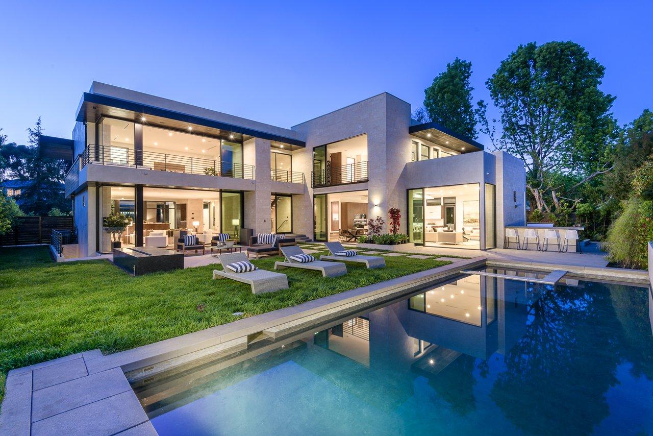 Modern residence with floor-to-ceiling glazing beside a reflecting pool at blue hour